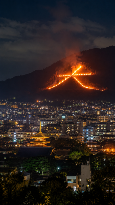 京都の夏の夜に山肌へ大文字の炎が浮かび上がり京都市街を照らす五山送り火の風景