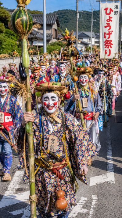 香川県高松市香川町浅野でひょうげ祭りが行われ、色鮮やかな化粧と奇抜な衣装を身につけた人々が農作物で作った神具を手に練り歩く伝統行事の風景