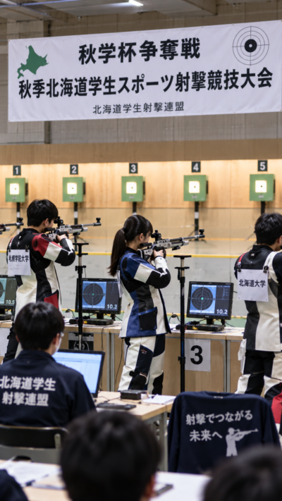 北海道札幌市の宮の沢屋内競技場で秋学杯争奪戦・秋季北海道学生スポーツ射撃競技大会が開催され、学生射手がライフルを構えて標的を狙い、静かな射撃場で真剣に競技するスポーツ射撃の風景