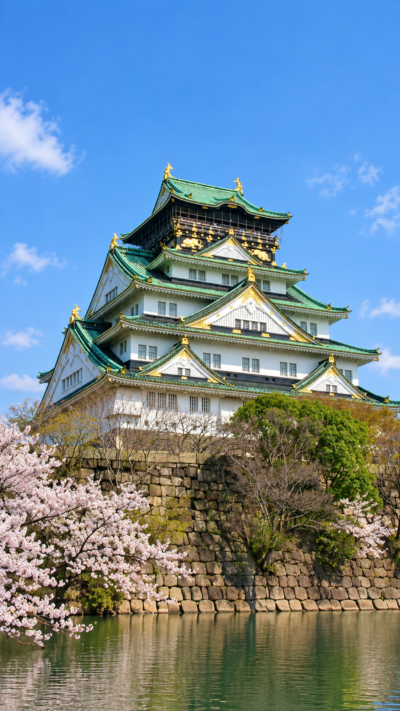 巨大な石垣と堀に囲まれた大阪城の天守閣が青空の下にそびえる壮大な城郭の風景