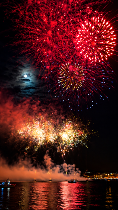 神奈川県横須賀市鴨居の港で夜空に大輪の花火が打ち上がり、海面に光が映る夏祭りの風景