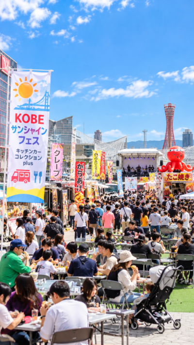 神戸でKOBEサンシャインフェス～キッチンカーコレクションplus～が開催され、さまざまなキッチンカーや飲食ブースが並び、多くの来場者がグルメやステージを楽しむイベントの風景