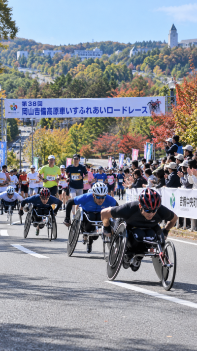 岡山県吉備中央町の吉備高原都市で第38回岡山吉備高原車いすふれあいロードレースが開催され、競技用車いすの選手や一般ランナーが多くの観客の声援を受けながら秋のコースを走るスポーツ大会の風景